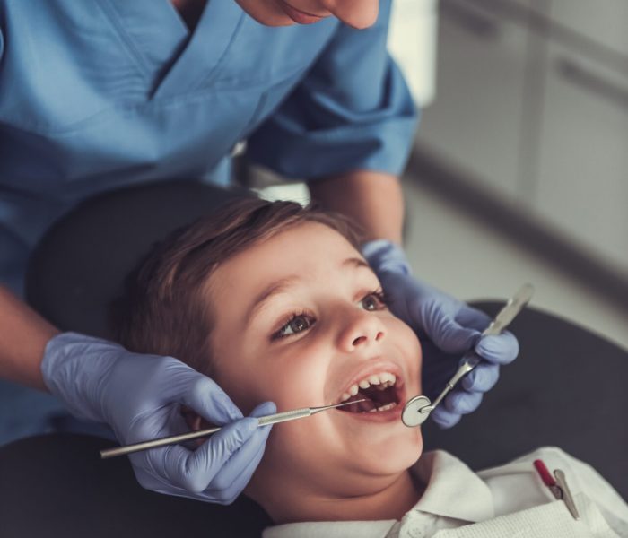 Cute little boy is sitting in chair while visiting beautiful young dentist