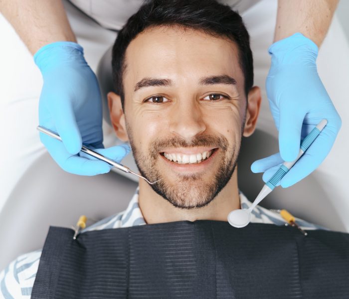 Smiling young man sitting in dentist chair while doctor examining his teeth